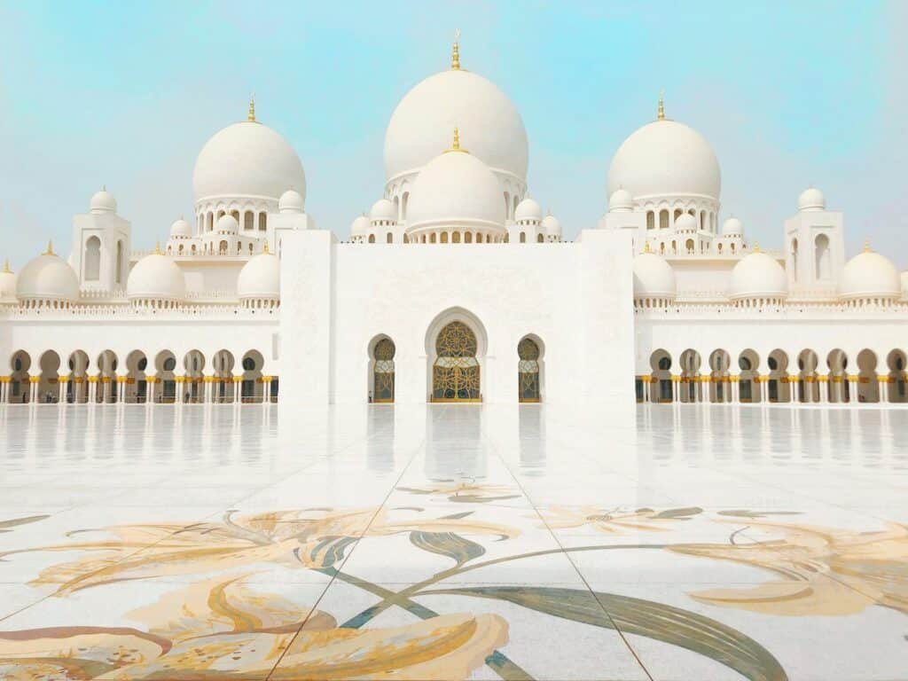 Mesquita Sheikh Zayed em Abu Dhabi, de fachada branca com grandes cúpulas e intrincados padrões florais no pátio sob um céu claro, vista de frente que pode ser visitada com o eSIM Emirados Árabes Unidos.