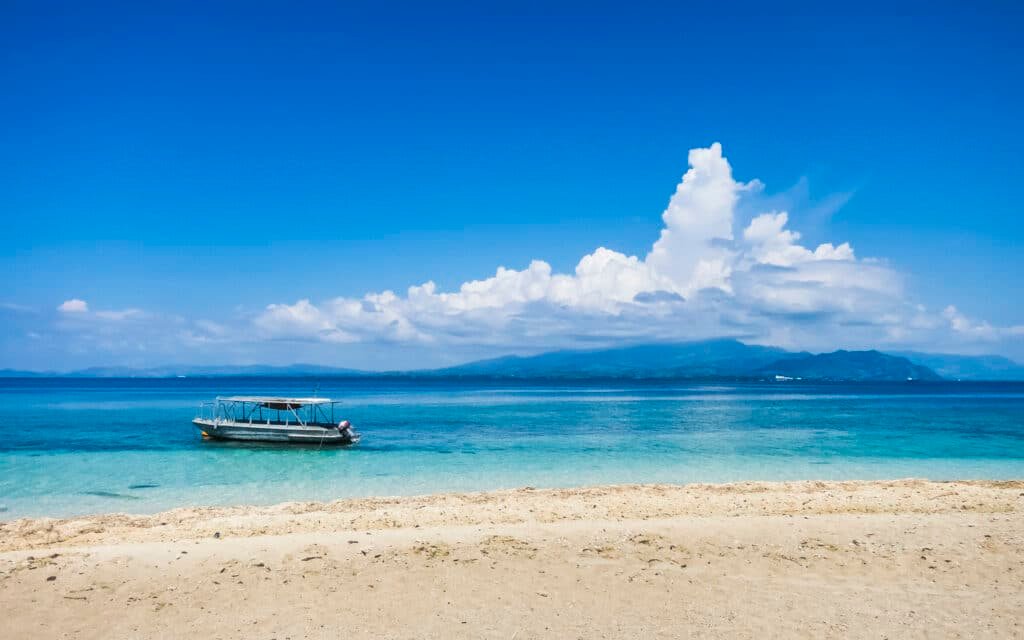 vista de um barco na praia da Ilha Viti Levu, com areias brancas e águas azuis cristalinas, com céu muito azul com nuvens, para ilustrar o texto de chip celular Fiji