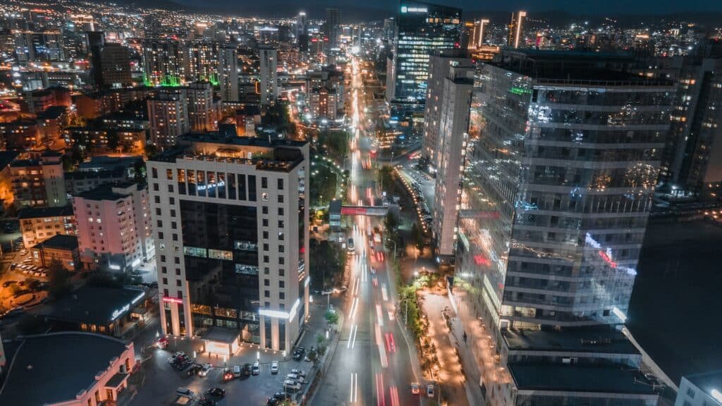Uma avenida muito movimentada no centro da capital da Mongólia com prédios espelhados, carros passando, muitas luzes acessas por ser de noite