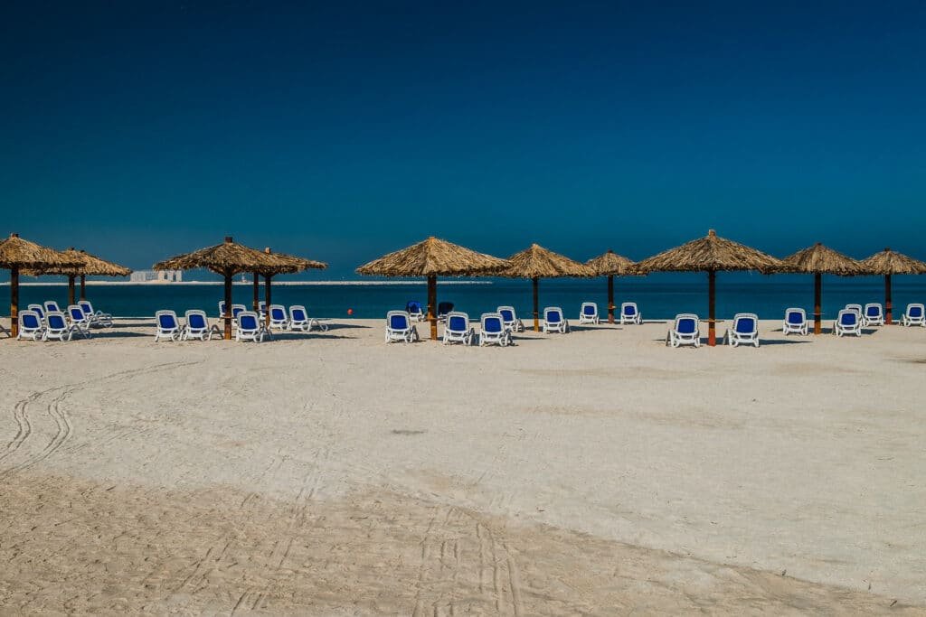 Praia de Al Jazeerah com uma extensa faixa de areia com guarda-sóis de palha e cadeiras azuis e brancas embaixo deles, para representar o que fazer em Ras Al Khaimah
