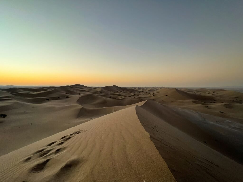 Uma vasta paisagem desértica do Lut Desert em Kerman com dunas de areia sob um céu claro e escuro.