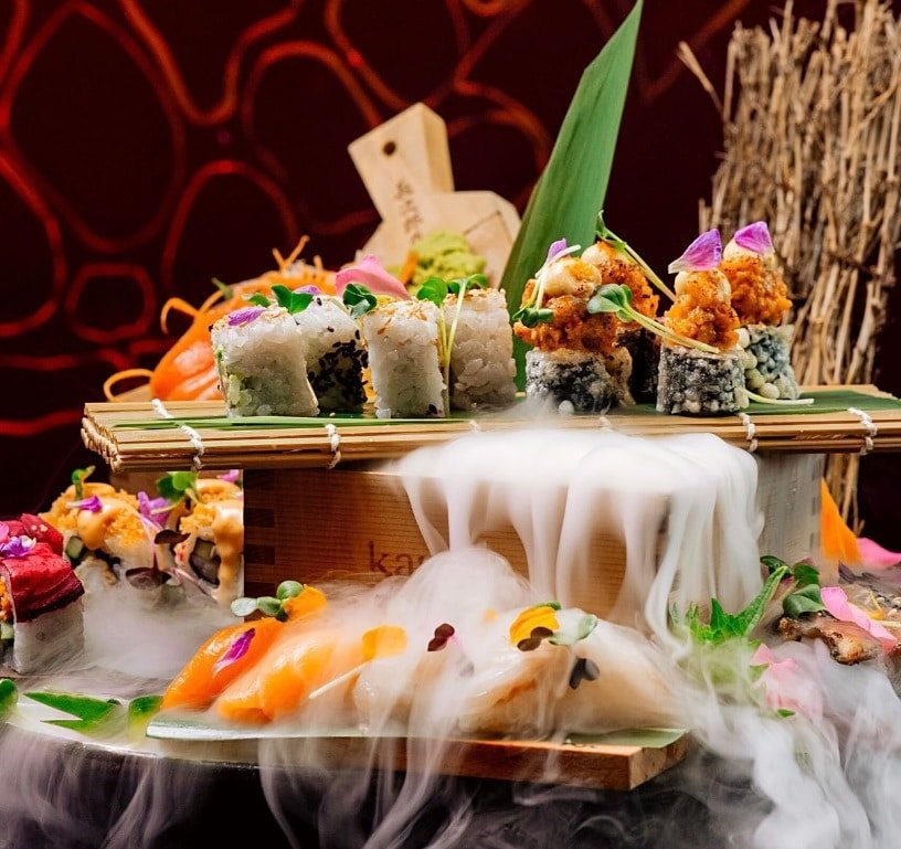 Uma mesa com alguns sushis, peixes crus e outros pratos servidos no restaurante Karma Kafé Rak by Buddha