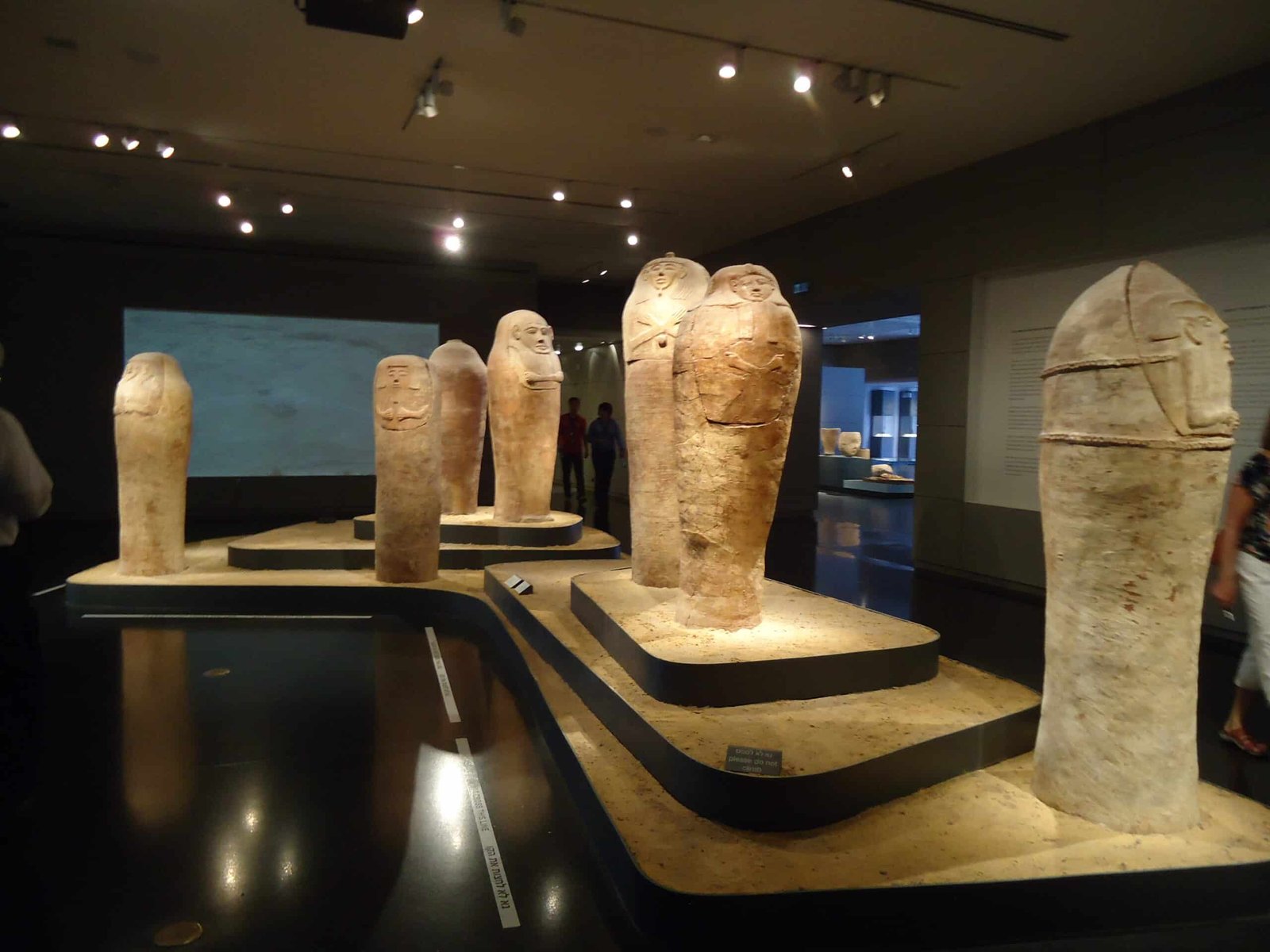 Uma exposição de museu com diversas estátuas de pedra antigas fica em uma sala com iluminação quente no Museu de Israel.