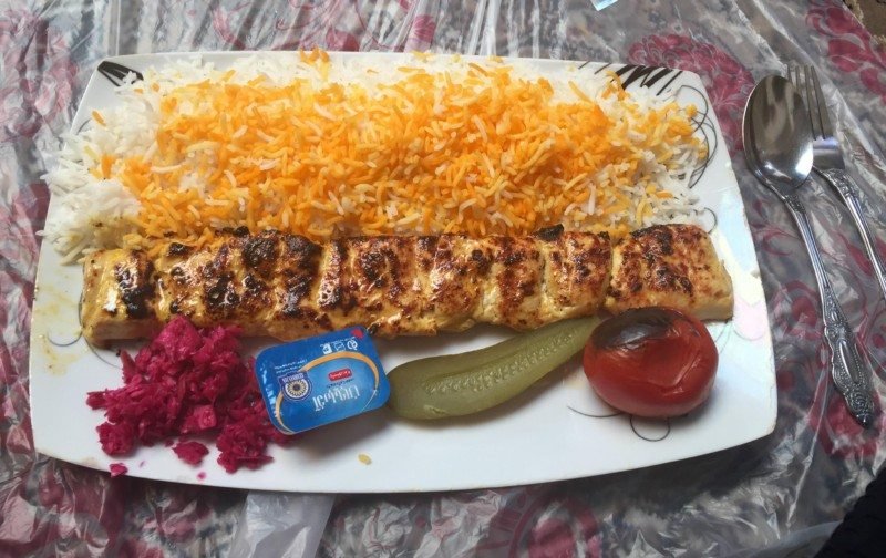 Imagem de um prato típico chamado Chelo kabab, ele é comporto por arroz, um pedaço de carne e vegetais.