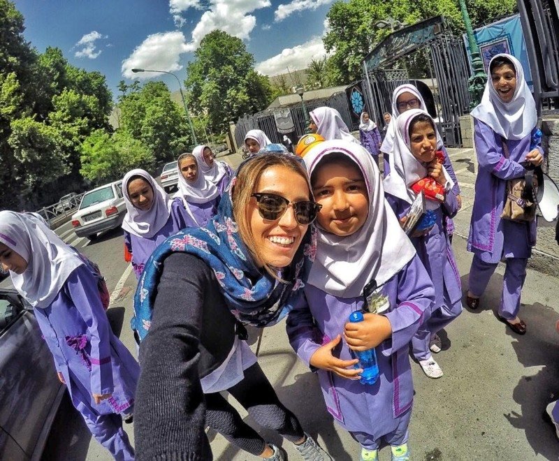 Imagem de uma mulher com uma menina com lenço na cabeça durante o dia e ao fundo várias meninas com lenço na cabeça.