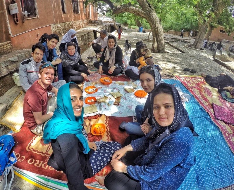Imagem de mulheres e homens sentados  no chão comendo, as mulheres estão usando lenço cobrindo os cabelos durante o dia. Representa Irã.